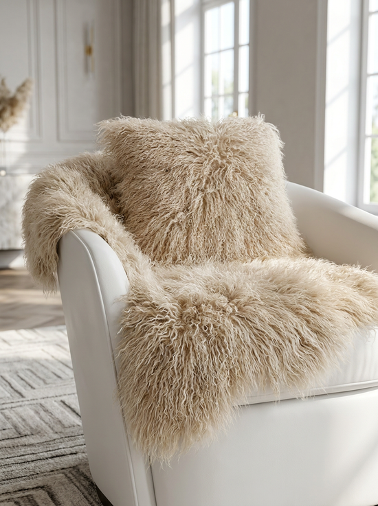 Beige sheepskin cushion on a white armchair, showing the curly pile and soft texture.