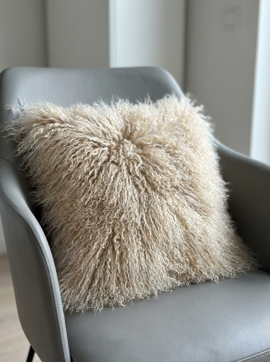 Beige sheepskin cushion on a grey armchair, with a dense curly fur surface in the foreground.