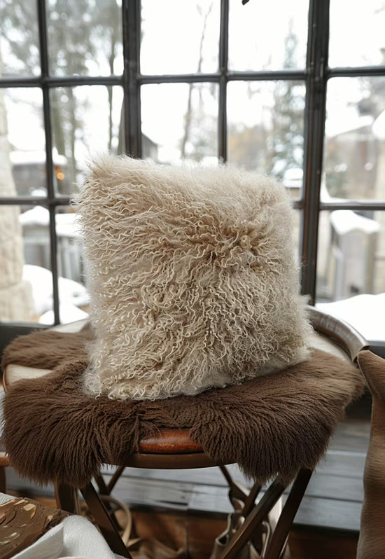 Beige sheepskin cushion on a chair by the window, with a curly fur texture and a brown base layer.