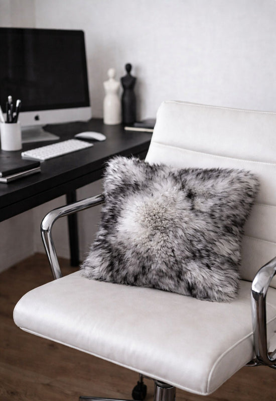 Grey sheepskin cushion on a white office chair in front of a desk and monitor.