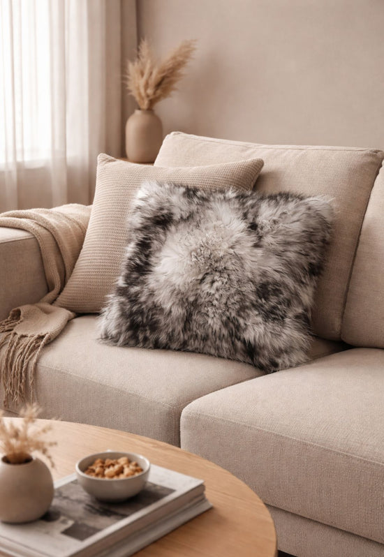 Grey sheepskin cushion on a light sofa with other cushions and a throw in a living room.