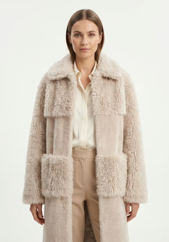 Beige sheepskin coat for women on model with visible shearling sections, shirt and trousers underneath.
