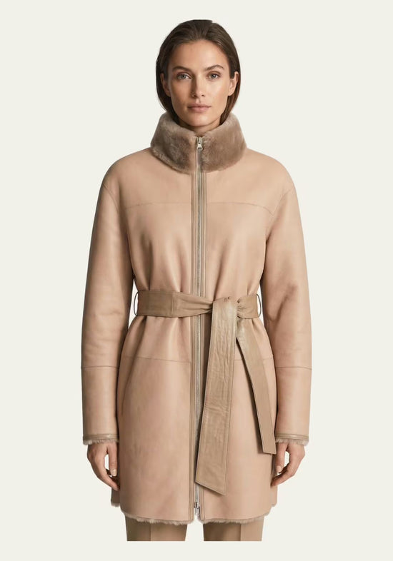 Beige women's sheepskin coat shown frontally, with stand-up collar, zip fastening and belt.