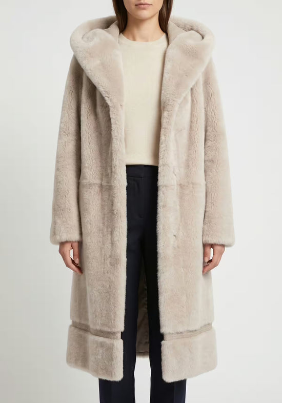 Women’s sheepskin coat in cream-beige with hood, worn closed at the front on a woman.