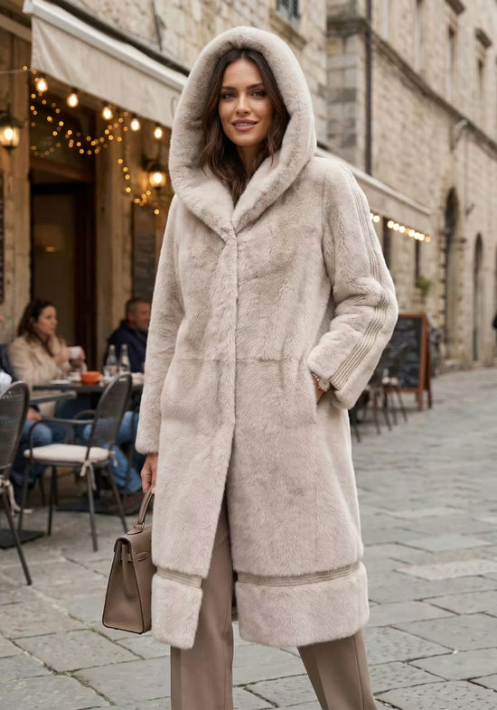 Women’s sheepskin coat in cream-beige with hood, worn at the front with the hood up.