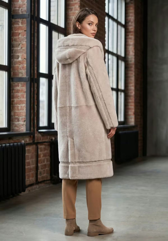 Women’s sheepskin coat in cream-beige with hood, seen from behind on a woman in the city.