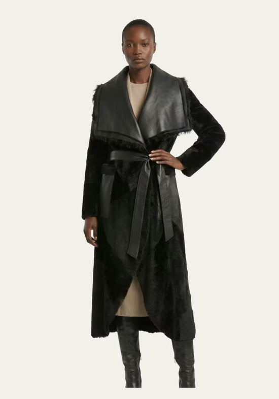 Black women’s sheepskin coat worn on a model, open at the front with a tie belt.