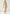 Women’s sheepskin coat made from curly sheepskin in cream-beige, full-length front view worn with trousers and boots.