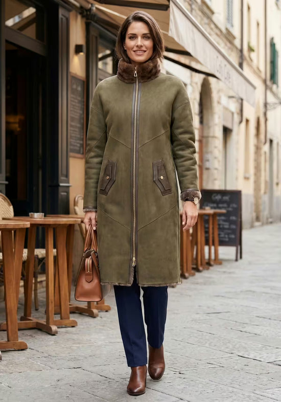 Ladies' sheepskin coat in olive worn in a city setting, open with boots, bag and visible sheepskin collar.