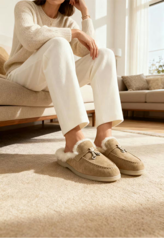 Women's sheepskin mules in sand worn indoors, with the sheepskin lining visible.
