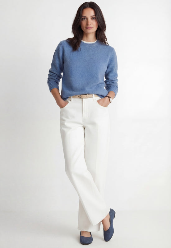 Women's light blue cashmere sweater shown worn with hands in pockets and white trousers.