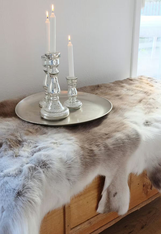 Reindeer hide in cream and brown as a decorative hide on a wooden bench with candleholders on a tray