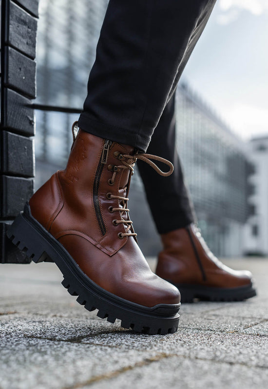Męskie buty uliczne z owczej skóry w brązie, noszone na jednej nodze na zewnątrz.