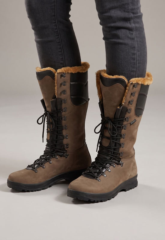 Brown sheepskin hiking boots worn as a pair on the legs, with black lacing in a studio setting.