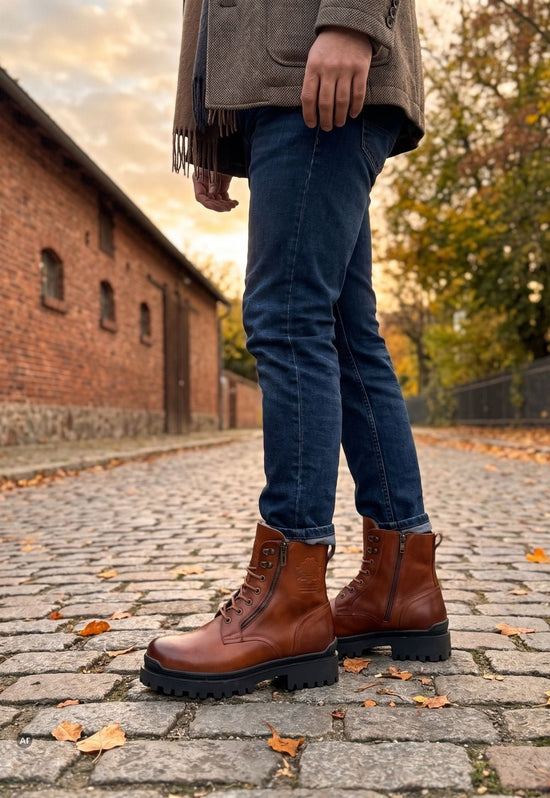 Brown men's sheepskin ankle boots worn outdoors with jeans on cobblestones.