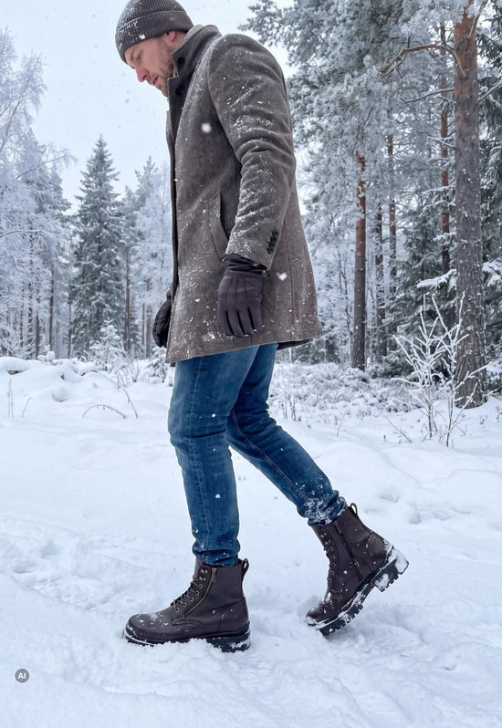 Dark brown men’s sheepskin ankle boot in leather, worn in the snow with coat and jeans.