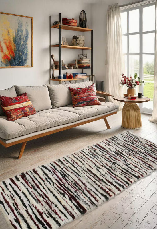 Sheeps wool rug in multicolour in a bright living room in front of a sofa, shelf and window