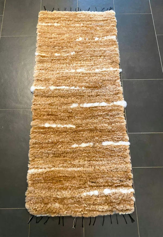 Honey-coloured wool runner from above on dark tiles, with a visible texture.