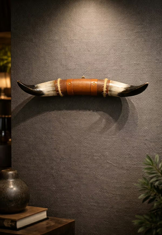 Bull horn wall decoration with leather and wooden holder on a textured wall, styled in a living space with decor.