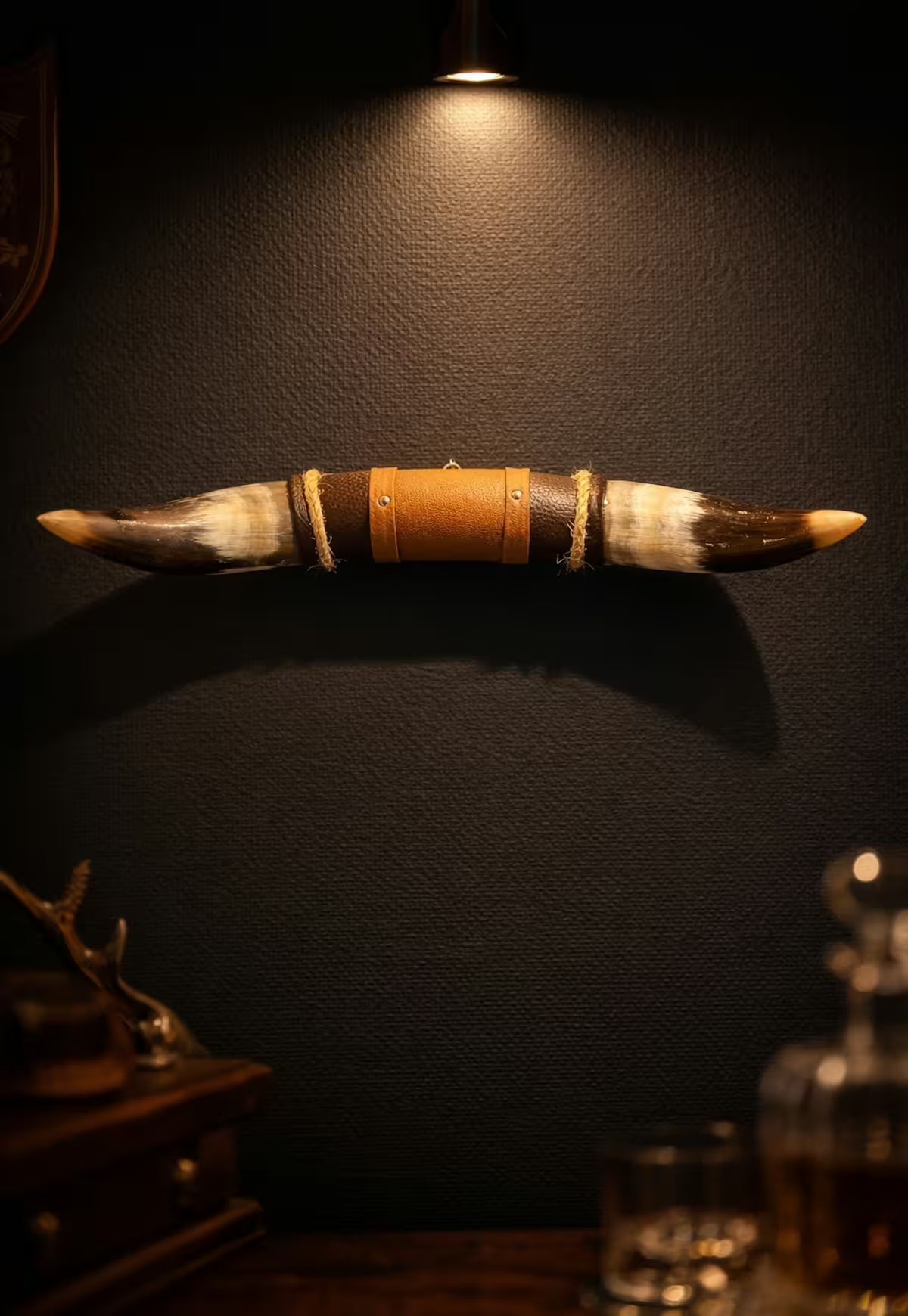 Wall decoration made of natural horn with leather and wood holder, front view on a dark wall with spotlight.