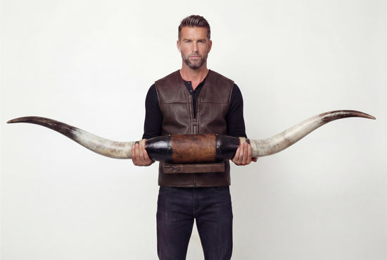 Man is holding a black leather wall decoration with long longhorns from the front.