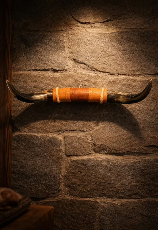 Bull horn wall decoration made from natural horn with a leather and wood holder on a stone wall.