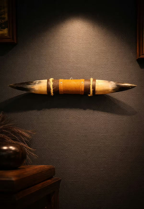 Wall decoration made of natural horn with leather and wooden bracket on a dark wall, photographed in warm light.