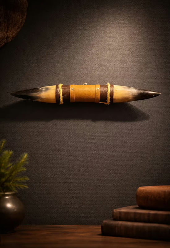 Wall decoration made of natural horn with leather and wooden bracket, shown frontally on a dark wall.