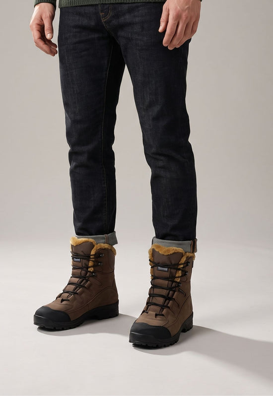 Men’s legs in the studio wearing brown sheepskin hiking boots, jeans and a black sole.