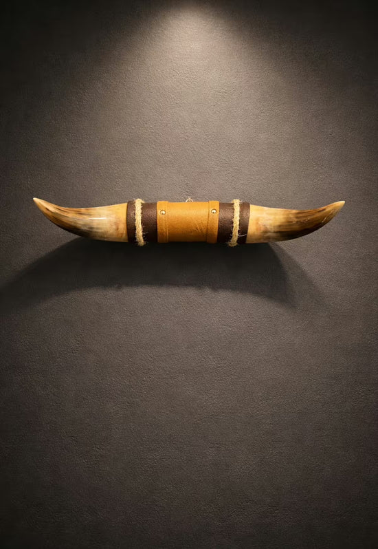Horn wall object with brown leather holder and wooden details, staged on a dark wall.