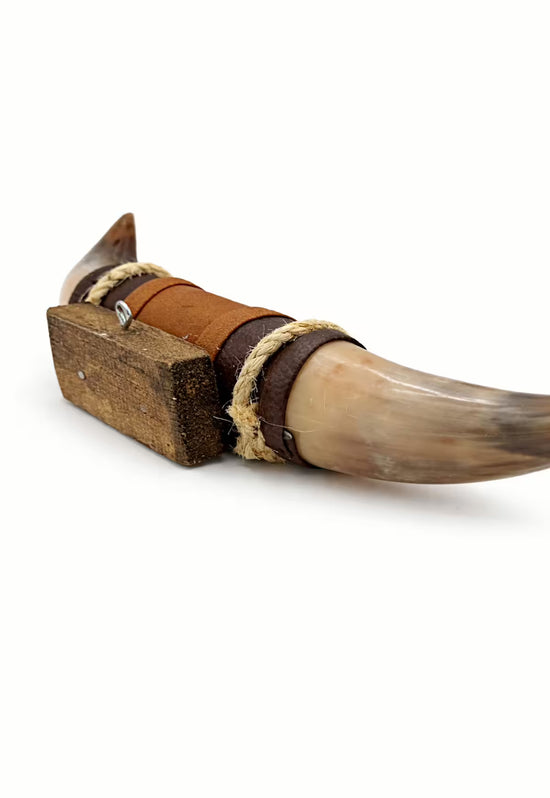 Detail of a horn wall object with leather wrapping, wooden holder and visible horn tip.