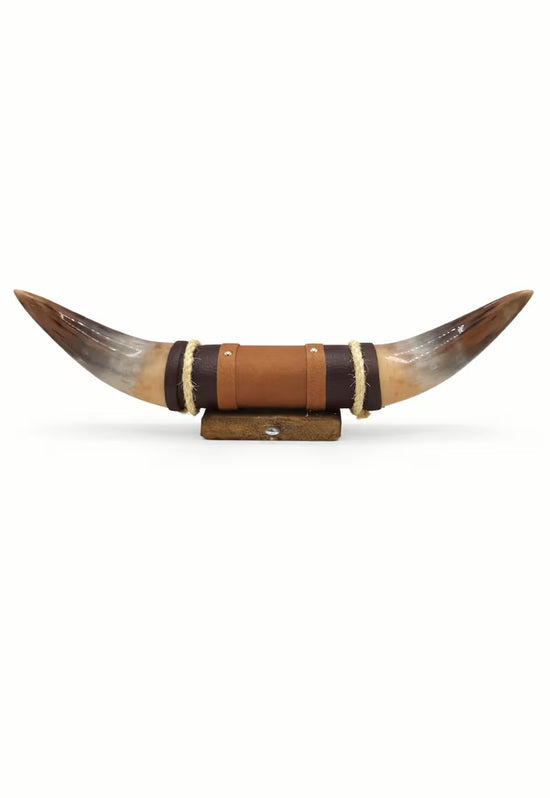 Cut-out horn wall object in brown with leather wrapping and wooden holder, front view.