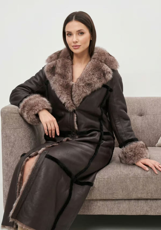 Reversible women’s sheepskin coat in espresso, worn seated with an open cut and fur collar.