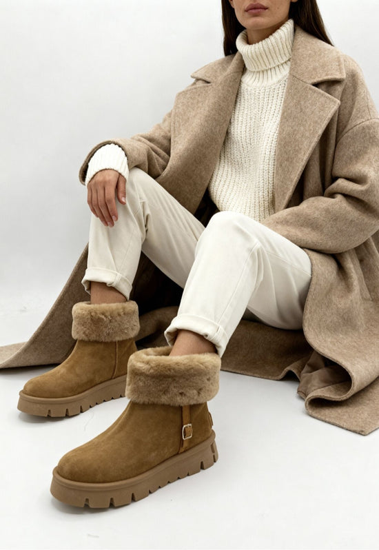Women's brown shearling winter boots worn with a coat and light trousers